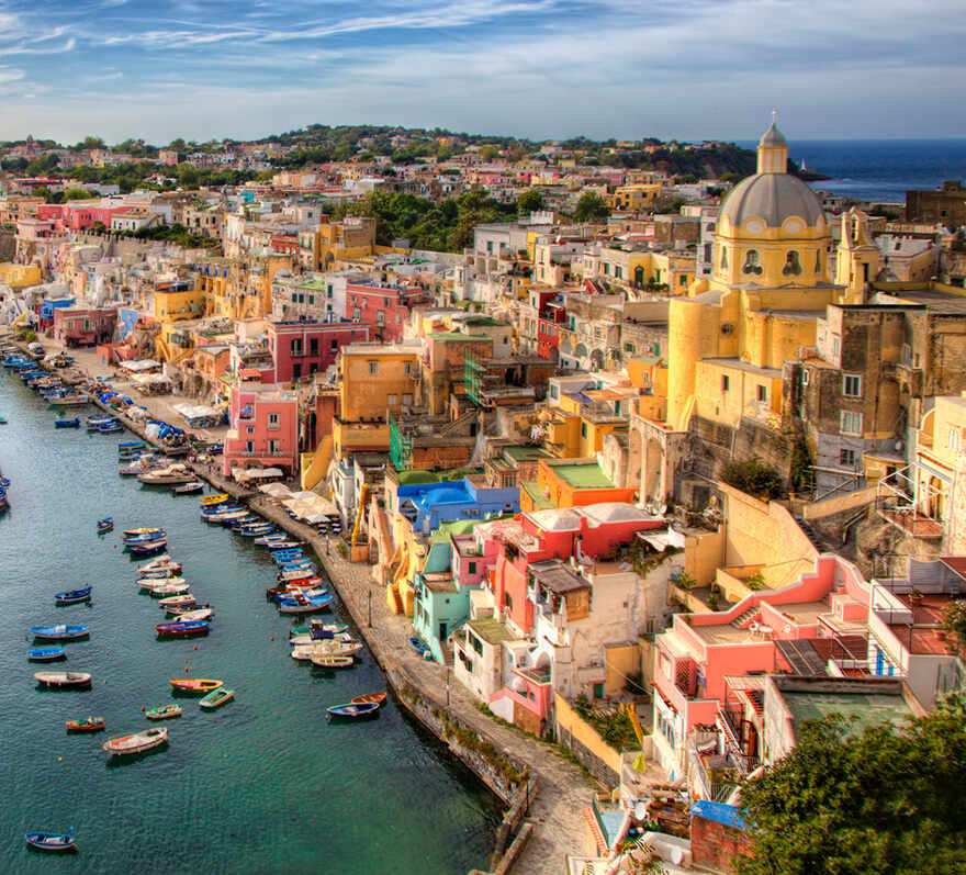 Aerial view of the coastal town of Salerno featuring brightly colored buildings, a large domed church, and boats docked along the waterfront.