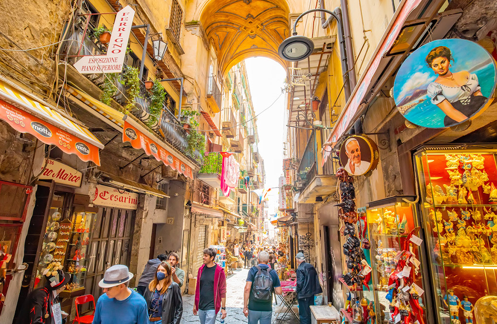 Tourists stroll through a narrow city street, surrounded by charming buildings and vibrant local culture.